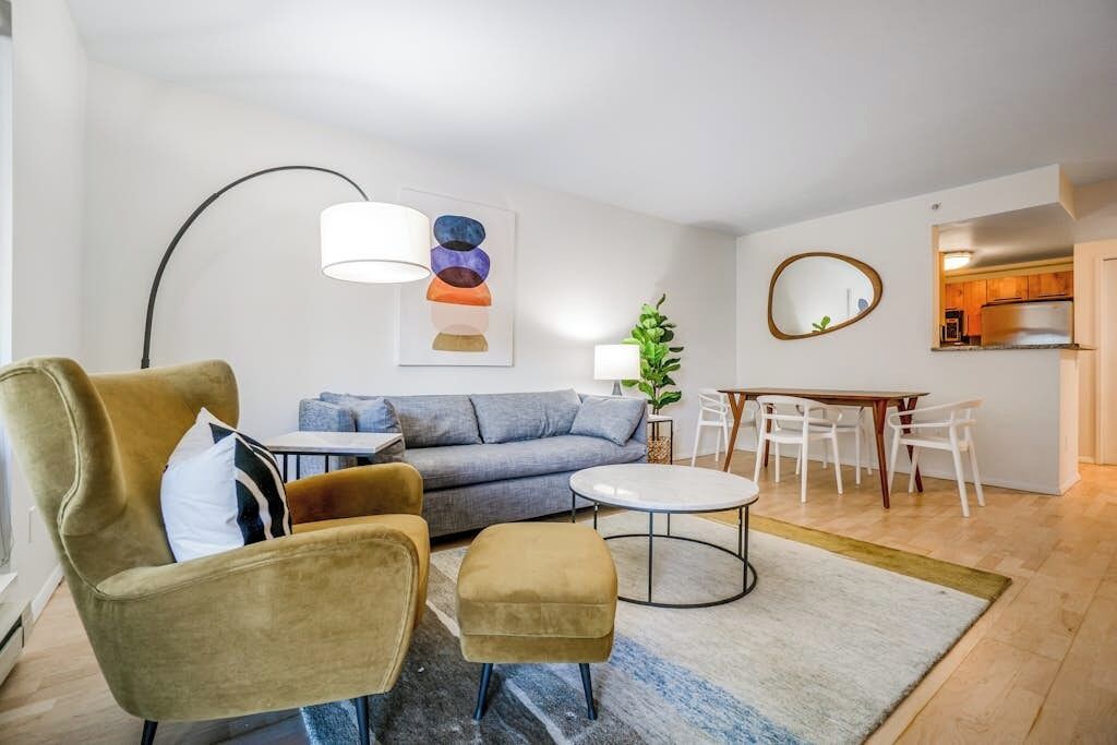 Un salon moderne comprenant un canapé, un fauteuil, un pouf et une table à manger avec des chaises.