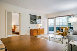 A modern hotel room with a wooden dining table, a sofa, a small armchair, a cabinet, and a large window offering a view. - Amazing 1BR Washington State Conv. Center Dog Frie (Seattle)