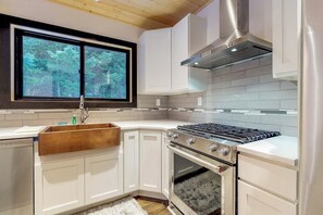A kitchen with white cabinets, a stainless steel stove, and a window overlooking a forest. - Stylish 3BR - Fireplace - Deck - Washer Dryer (Cle Elum)