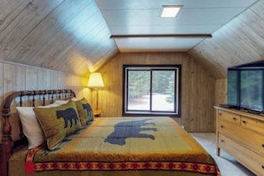 A bedroom with a wooden ceiling, a bed with a patterned bedspread, a nightstand with a lamp, a dresser, and a television. - Stylish 3BR - Fireplace - Deck - Washer Dryer (Cle Elum)