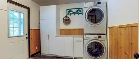 Een wasserette met twee gestapelde wasmachines, houten kastjes, een deur met raam en een wandrek voor het drogen van was.