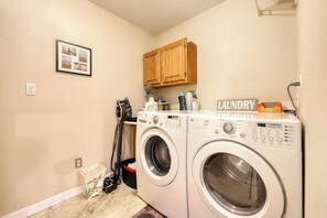 A laundry room with two front-loading washing machines, a wooden cabinet above, and a framed photo on the wall.