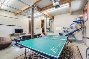 Ein Zimmer mit einer Tischtennisplatte, einem Fernseher, einem Fahrrad und einer Treppe.