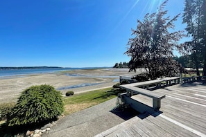 Una terraza de madera con un banco que da a una playa con cielo despejado.