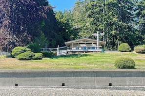 Un edificio con un porche cubierto y un asta de bandera, rodeado de árboles y un área verde.