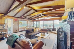 A spacious living area with a high ceiling, wooden beams, a sofa, a coffee table, and a view through large windows. - 3 BR Waterfront home in the heart of Gig Harbor (Gig Harbor)