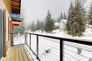 A wooden deck with a metal railing, overlooking a snowy landscape with trees and a house. - 3BR all-season cabin with deck - walk to the lifts (Snoqualmie Pass)
