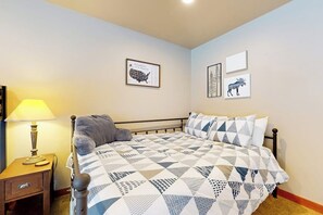 A bedroom with a bed, a nightstand, a lamp, and wall art including a map and animal illustrations. - 3BR all-season cabin with deck - walk to the lifts (Snoqualmie Pass)