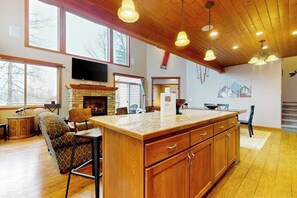 A spacious living room with a large wooden island, a fireplace, and a television mounted on the wall. - 3BR all-season cabin with deck - walk to the lifts (Snoqualmie Pass)
