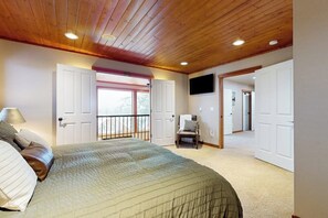 A bedroom with a large bed, a chair, a television, and a balcony. - 3BR all-season cabin with deck - walk to the lifts (Snoqualmie Pass)