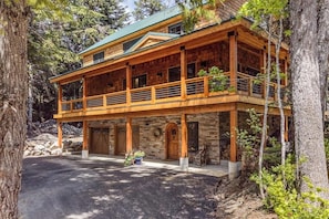 A two-story log cabin with a balcony, stone foundation, and a driveway leading to the entrance. - 3BR ski In and Out access, indoor sauna, & fireplace (Snoqualmie Pass)