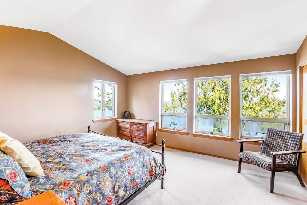 Un dormitorio con cama, cómoda, silla y ventanas.