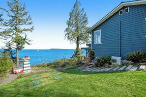 A house with a view of the sea, a small dock, and a grassy yard.