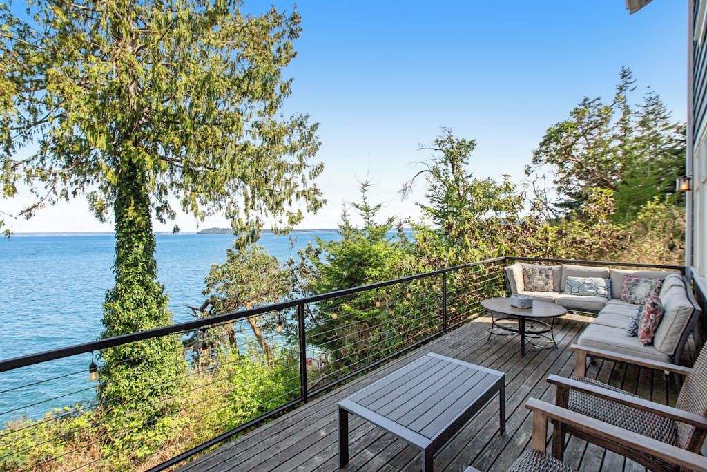 A deck with a sofa and table, overlooking a body of water.