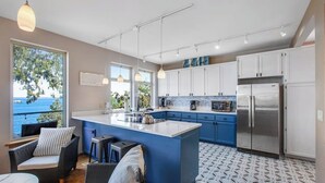 A modern kitchen with a large island, white cabinets, and a view of the sea.