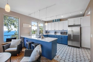 A modern kitchen with a large island, white cabinets, and a view of the sea.