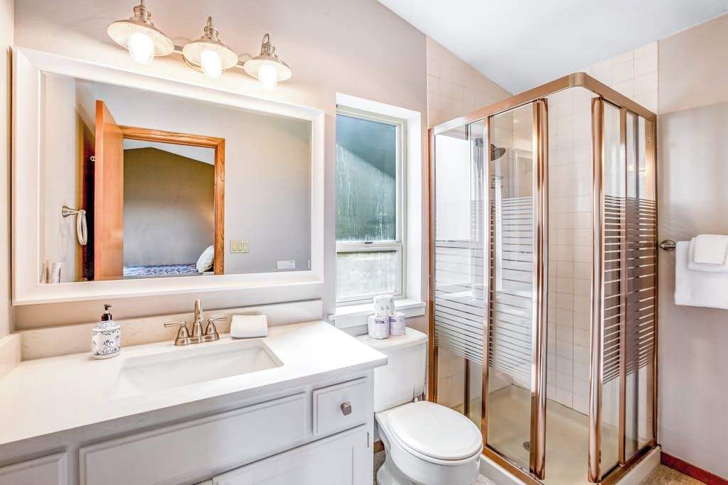 A modern bathroom with a white sink, a mirror, a toilet, and a glass-enclosed shower.