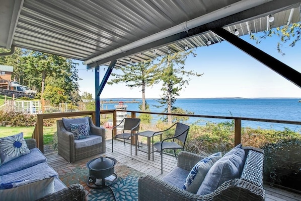 An outdoor deck with wicker furniture and a view of the sea.