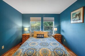 A bedroom with a large bed, two bedside tables, and a window with blinds.