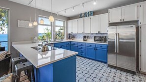 A modern kitchen with a large island, blue cabinets, and a stainless steel refrigerator.