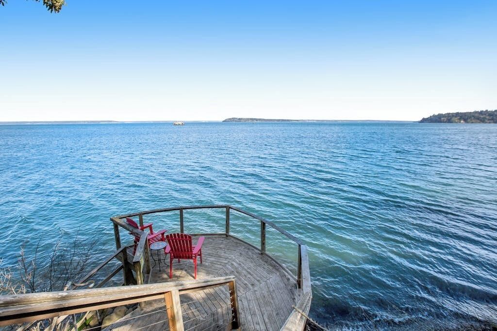 Un muelle de madera con barandilla y dos sillas rojas que dan a una superficie acuática tranquila.