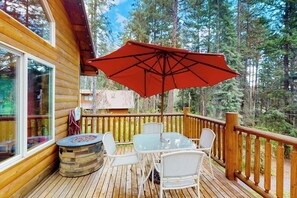 Eine Holzterrasse mit Tisch und Stühlen, einem Sonnenschirm und einer Feuerstelle aus Stein.