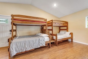 Ein Zimmer mit zwei Etagenbetten, Holzboden, einer weißen Tür und einem Fenster mit Jalousien.