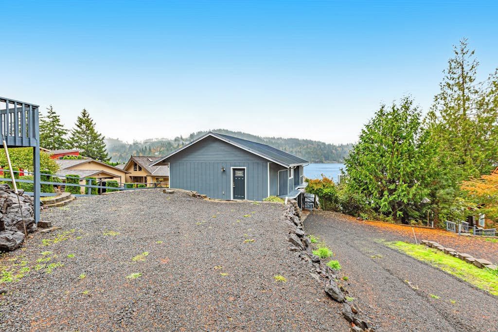 Un immobile residenziale con vialetto sterrato, terrazza in legno e una casa con tetto grigio.