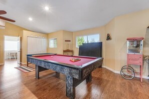 A pool table in a room with wooden floors, a window, and a popcorn machine. - 1BR lakefront guest house with kayaks & game table (Olympia)