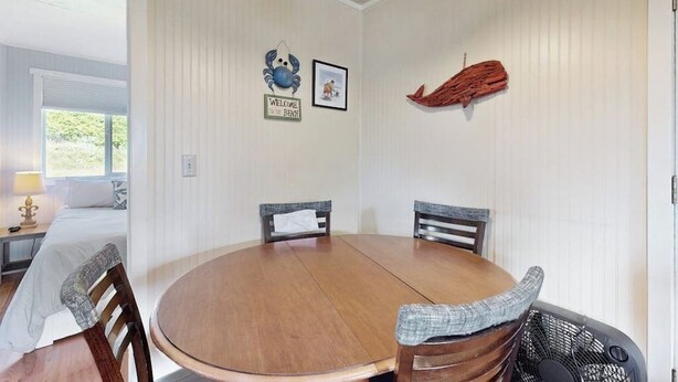 A room with a round wooden table, two chairs, a bed with a white bedspread, a nightstand with a lamp, and a wall with a welcome sign and a framed picture. - 2BR Oceanview Dog Friendly | Deck | Fireplace (Moclips)