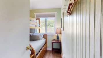 A room with bunk beds, a small bedside table with a lamp, and a window with blinds.