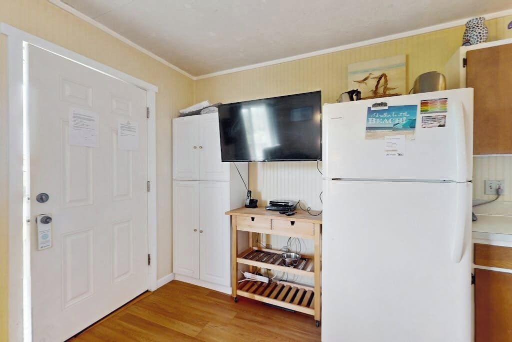 A compact kitchen with a refrigerator, a microwave, and a flat-screen TV mounted above the counter.