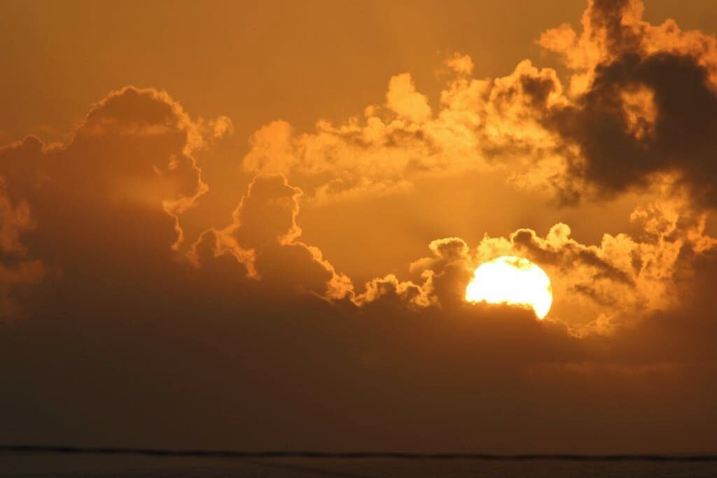 Un coucher de soleil avec des nuages et la silhouette d’une côte.