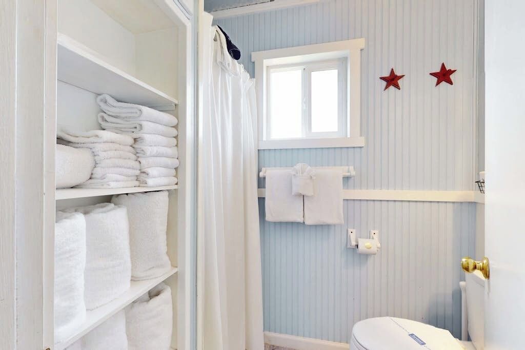Une salle de bain avec des toilettes blanches, une fenêtre et un porte-serviettes.