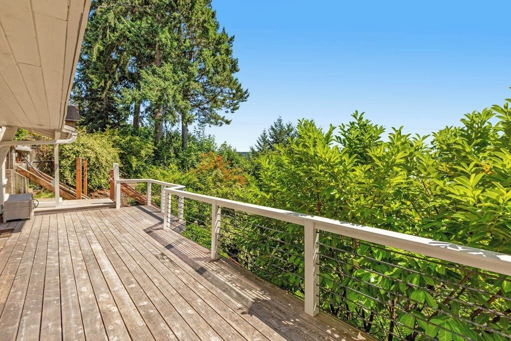 A wooden deck with a white railing, surrounded by lush greenery and trees.