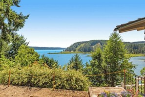 A view of a lake with a forested area and a building with a wooden deck. - Gorgeous 2BR Soundview - Balcony - Washer Dryer (Lilliwaup)