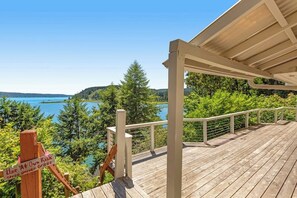 A wooden deck with a view of a lake and forest. - Gorgeous 2BR Soundview - Balcony - Washer Dryer (Lilliwaup)