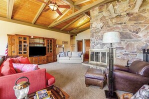 A spacious living room with a stone wall, wooden ceiling beams, a television, and leather sofas. - Gorgeous 2BR Soundview - Balcony - Washer Dryer (Lilliwaup)