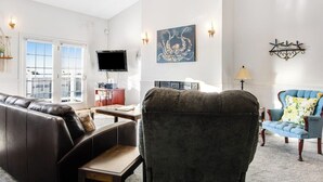 Una sala de estar con sofá, sillón, televisión y una obra de arte en la pared.