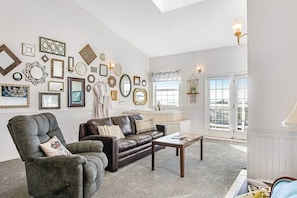 A living room with a brown leather sofa, a grey armchair, and a coffee table. - 1BR Oceanfront - Deck - Sauna - Fireplace (Ocean Shores)