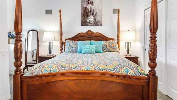 Una cama con dosel, un edredón estampado, un espejo, dos lámparas de noche y un cuadro en la pared.