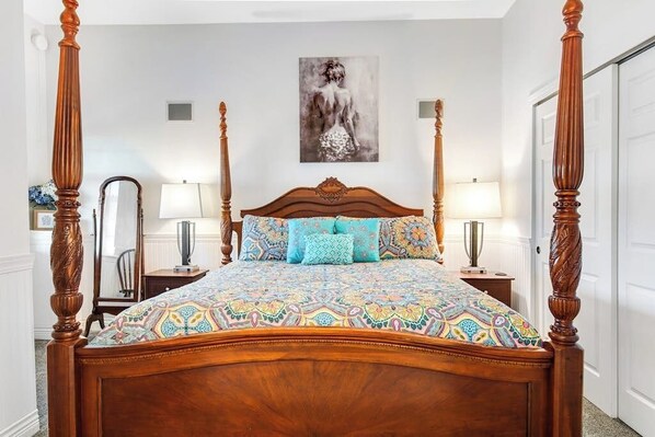 Un lit à baldaquin avec une couvre-lit à motifs, un miroir, deux lampes de chevet et un tableau accroché au mur.
