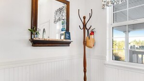 Una habitación con un banco de madera, un espejo, un perchero con cesta y una ventana con vistas.