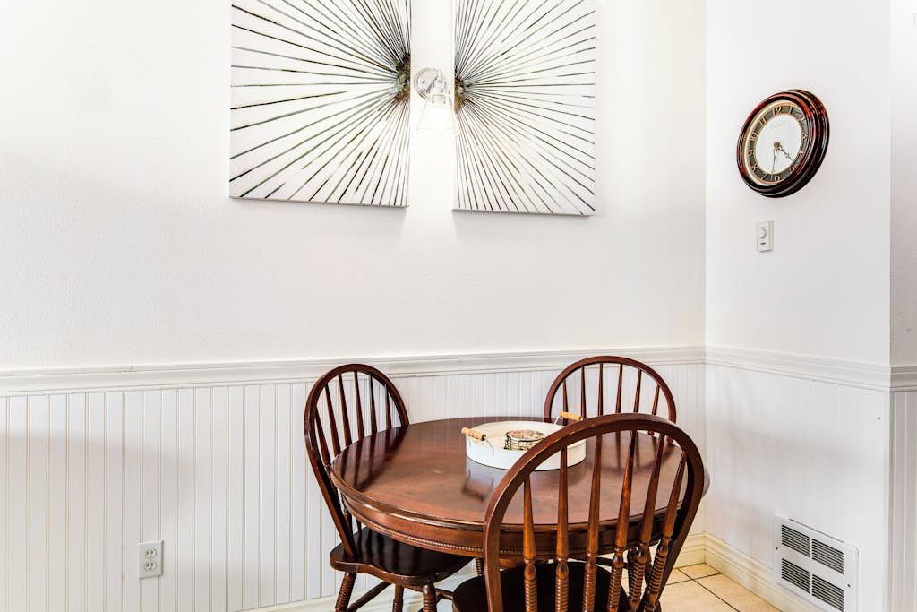 Un comedor con una mesa redonda de madera y cuatro sillas, un reloj en la pared y un adorno mural.