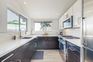 A modern kitchen with a large window, stainless steel appliances, and a dark wood cabinet. - Modern Waterfront Home with Amazing Views (Port Orchard)