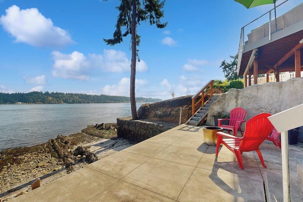 A concrete deck with a view of a lake, red chairs, and a staircase leading to a building.
