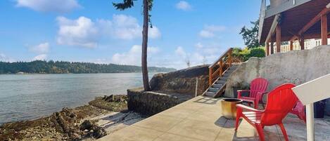 A concrete deck with a view of a lake, red chairs, and a staircase leading to a building.