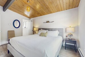 A bedroom with a large bed, a bedside table with a lamp, and a wooden ceiling. - Modern Waterfront Home with Amazing Views (Port Orchard)