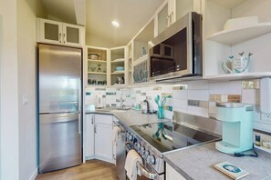 A modern kitchen with stainless steel appliances, white cabinetry, and a tiled backsplash. - Waterfront couples getaway with patio (Allyn)