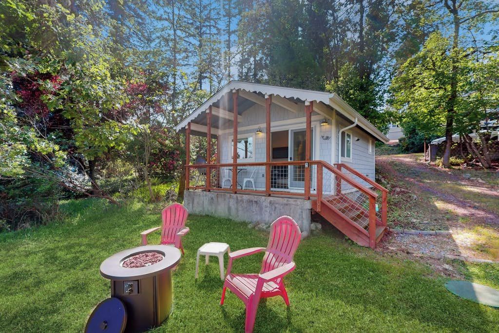 A wooden cabin with a porch, surrounded by a grassy yard and trees.